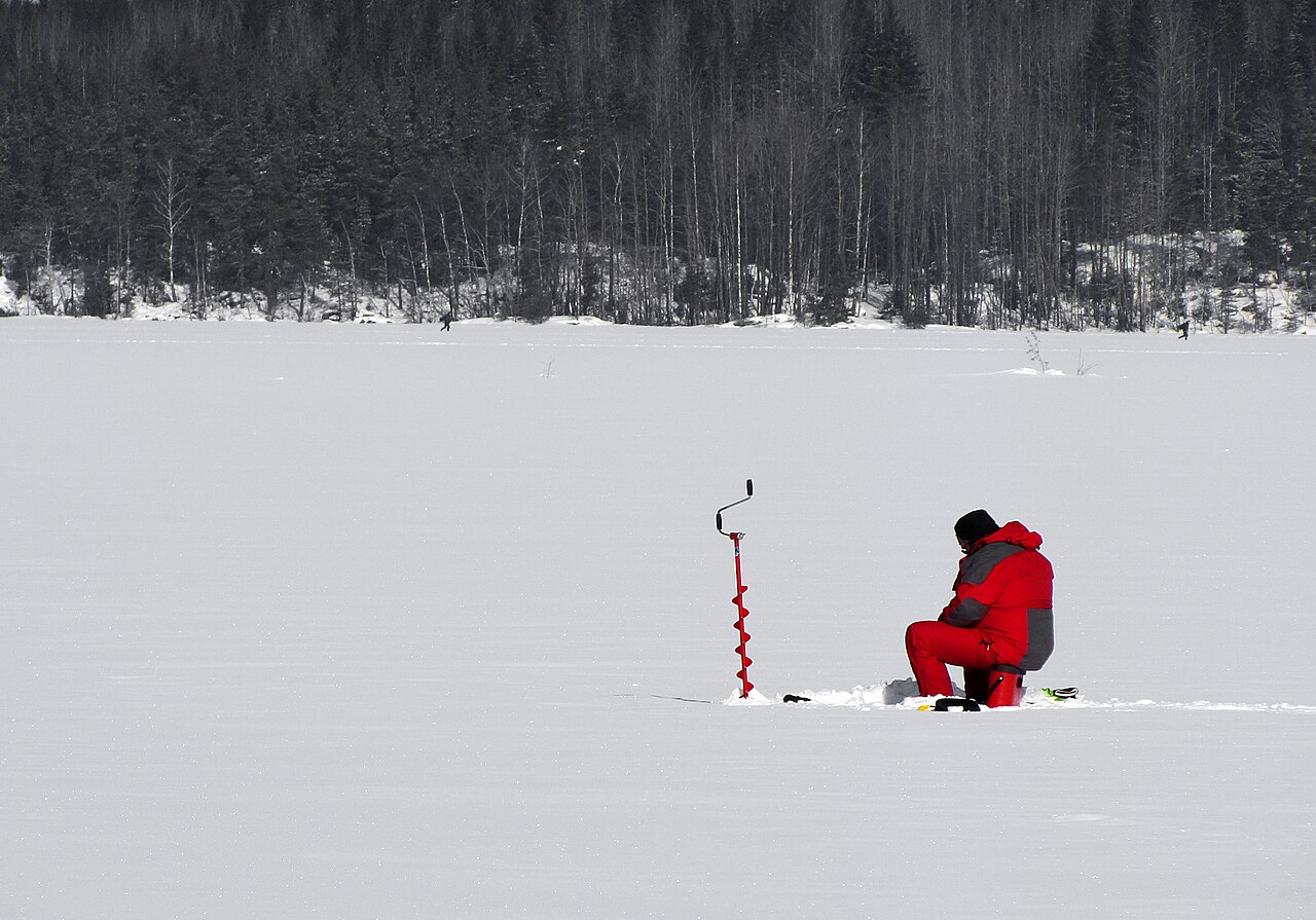Kayaker wearing a bright life jacket floating in a heat-conserving posture near the ice edge of a misty glacial lake