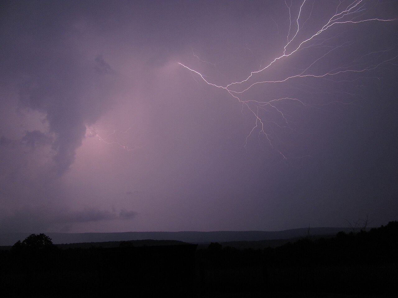 Hikers crouching low among boulders as lightning strikes a distant mountain ridge