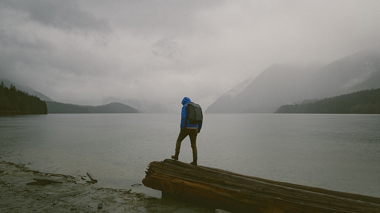 Hiker wrapped in an emergency bivvy beside a misty rainy mountain trail while a partner assists